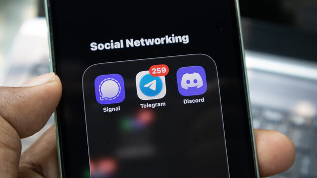 Handheld mobile phone showing Signal Telegram and Discord application icons inside social networking folder for communication.
