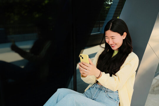 Young happy asian woman having video call in the street, holding phone