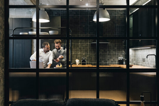Colleagues collaborating on mobile device in modern kitchen