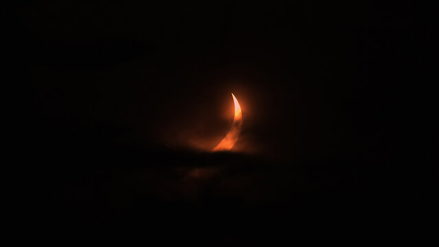 Eclipsed Sun Emerging Through Clouds