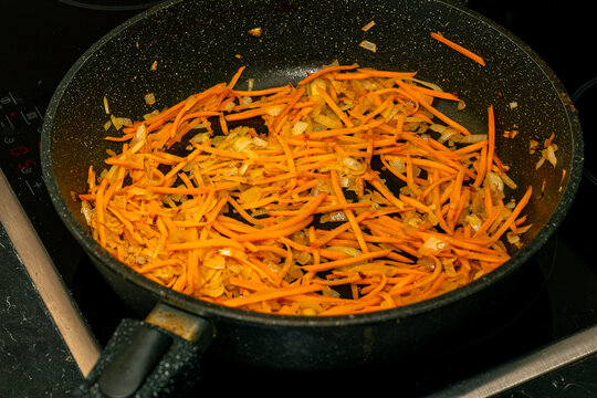 Sauteed shredded carrots and onions in a black frying pan on a stovetop, showcasing vibrant orange and yellow colors with a glossy finish