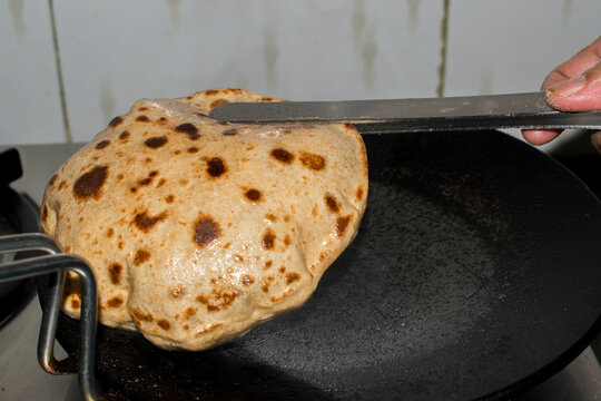 turning round paratha with kitchen tongs on a hot tawa,