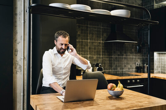 Professional working remotely, talking on phone in kitchen