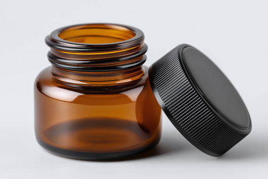Amber glass jar with black ribbed lid open on white surface, minimalist macro close up of empty supplement container with soft shadow and warm reflection