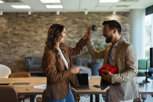 Colleagues celebrating business success with high five and gift