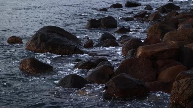 Ocean waves crashing against dark rocky coastline during a calm evening