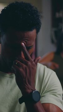 Annoyed African American husband holding face while wife nags in background indoors