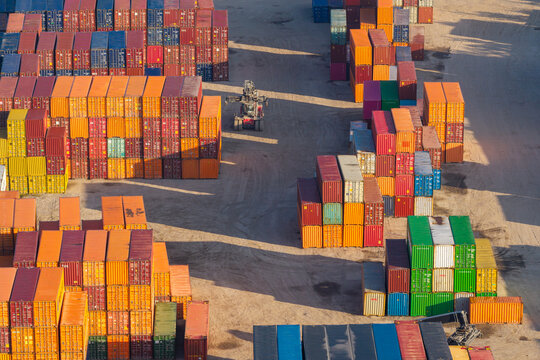 Aerial view of colorful shipping containers stacked in a large logistics hub with a reach stacker vehicle operating on the ground in Warszawa, Poland.