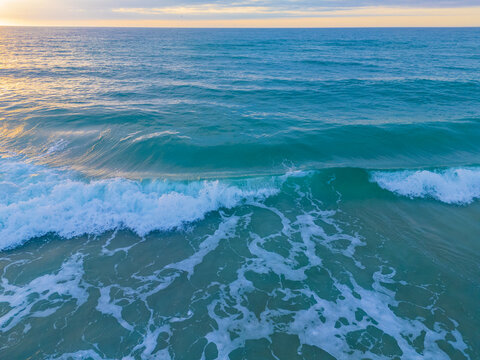 Aerial view of turquoise ocean waves with white foam rolling towards the shore near Crystal Pier, Wrightsville Beach, North Carolina, United States.