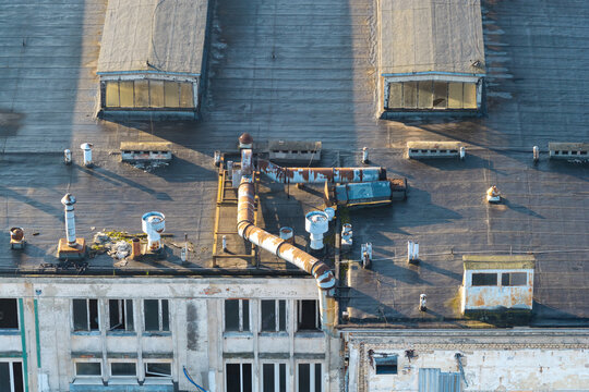 Aerial view of an old warehouse roof featuring weathered surfaces, rusted ventilation pipes, and skylights in Warszawa, Poland.