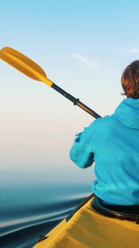 One person in a yellow kayak rowing with a paddle on still water under a clear blue sky. Morning adventure on the lake, showing an active outdoor lifestyle and water sports enthusiasm