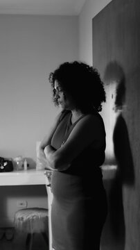 Sad and pensive middle-aged woman leaning against wall with crossed arms in black and white