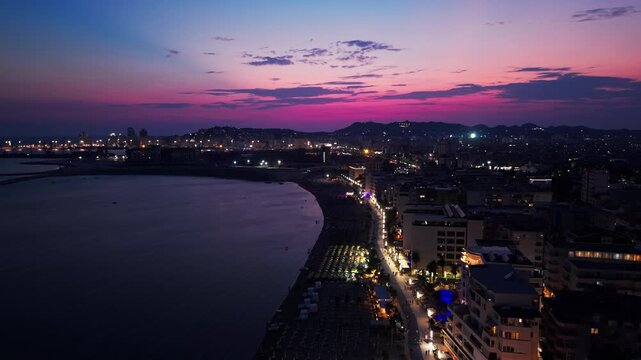 Durres, Albania &ndash; Aerial view of the illuminated beachfront promenade and beach in Durres at night, showing hotels, restaurants, beach umbrellas and urban development along the Adriatic Sea. 