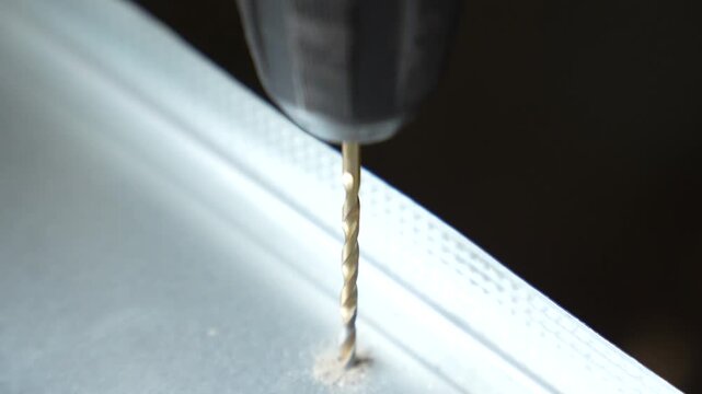 Close up of an electric drill making a hole in a metal drywall track