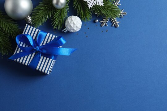 Top view of gift box with blue bow and Christmas decorations on blue background, space for text