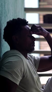 African American man sitting against wall with hand to forehead in deep contemplation