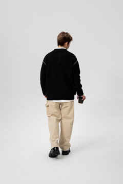 Back View of Young Asian Man Walking in Casual Streetwear Outfit with Coffee Cup on Minimalist Grey Studio Background