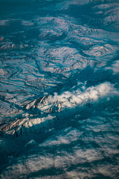 Aerial view of snow-covered mountains in the Scandinavian landscape, with rugged peaks, deep valleys, and scattered clouds under a clear sky in Oslo, Oslo, Norway.