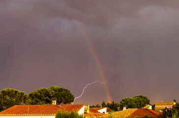 Obraz premium Un éclair d'orage croise l'arc en ciel au dessus du village