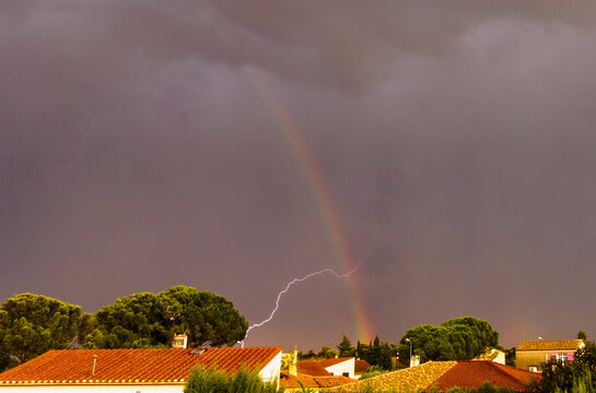Un &eacute;clair d'orage croise l'arc en ciel au dessus du village