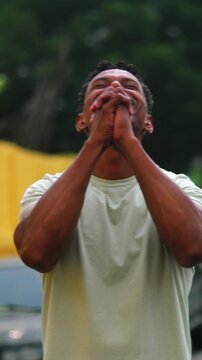 African American man smiling joyfully with clasped hands in outdoor prayer and gratitude