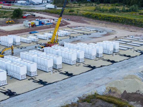 Aerial view of the BESS battery energy storage facility under construction with rows of white containers and a yellow crane on a gravel site in Trzebinia, Lesser Poland Voivode, Poland.