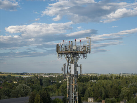 Aerial view of a telecommunication tower with antennas and relays rising above a lush green landscape under a blue sky with scattered clouds in Krakow, Lesser Poland Voivode, Poland.