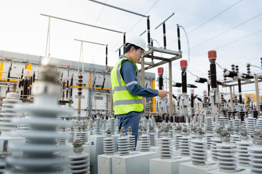 Inspecting capacitor units during a substation inspection, a technician reviews a tablet beside insulators and wires.