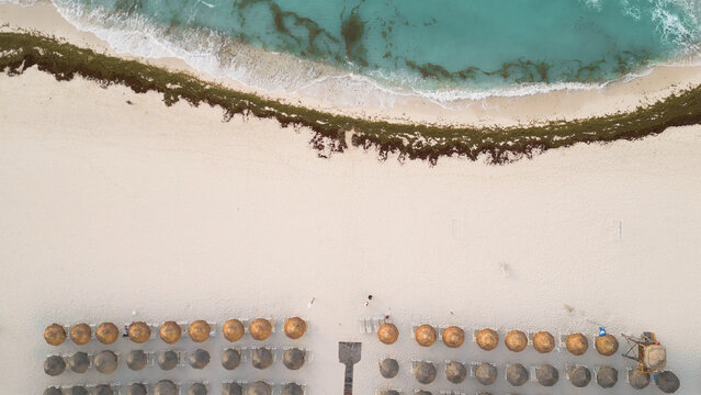 Aerial view of the white sand beach with rows of straw umbrellas and lounge chairs along the turquoise Caribbean Sea in Playa del Carmen, Quintana Roo, Mexico.