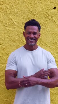 African American man standing with arms crossed smiling confidently against vibrant yellow wall