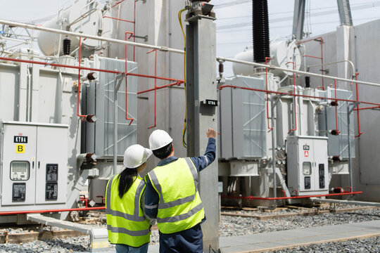 Transformer inspection at a substation shows two technicians beside a power transformer, one pointing up at the bushings and radiators.