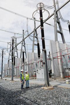 Scheduled power transformer inspection at the substation involves two technicians in hard hats checking a clipboard by the steel gantry.