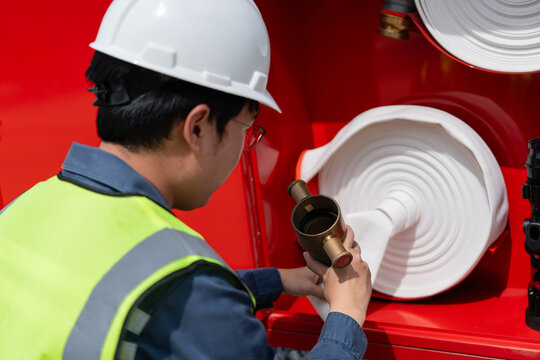 Fire protection system inspection shows a technician holding a nozzle connected to a white hose inside a red fire hose cabinet.