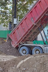 Red dump truck unloading soil and gravel at city road construction site  © Анна Хмеленок