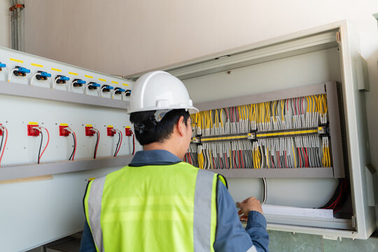 Routine substation inspection of a control cabinet is conducted by a technician wearing a hard hat, examining wires and terminals.