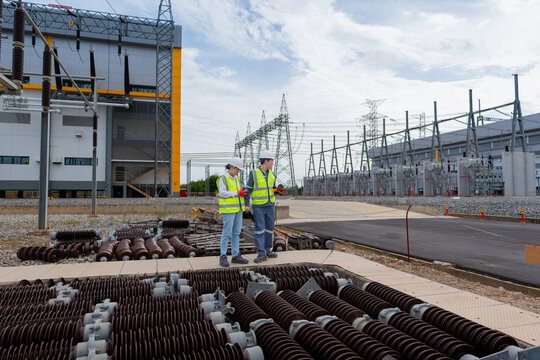 Scheduled decommissioned asset inspection of the porcelain insulator involves two engineers in hard hats sharing a tablet near the tower.