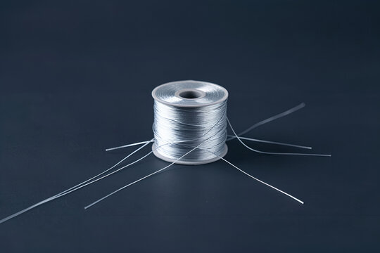 Single spool of fine silver thread on charcoal surface with branching light lines