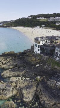 Cinematic vertical aerial view revealing rugged coastal rocks, tidal pools, and wild nature exposed during low tide in St Ives, Cornwall.
