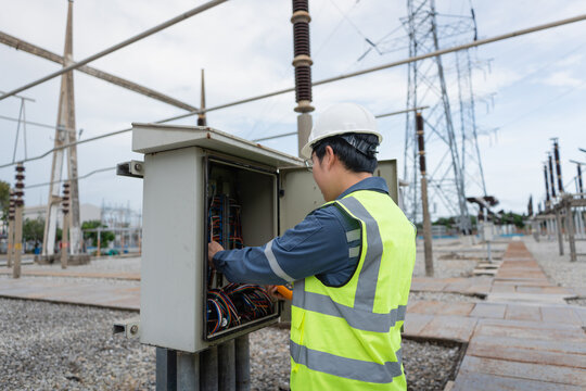 In a substation switchyard, cabinet inspection is underway as a technician checks wiring inside the control cabinet near a transmission tower.