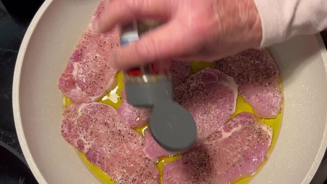 Seasoning raw meat cutlets in pan with pepper shaker