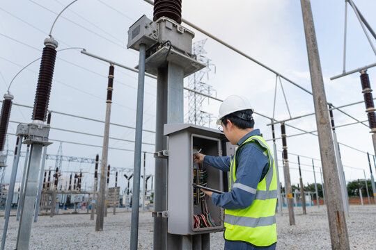 Control cabinet inspection occurs at a substation as an engineer uses a tablet to examine terminal wiring under a lattice tower.