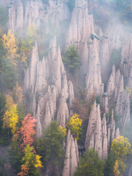 Aerial view of the earth pyramids in the Dolomites, featuring tall, slender rock formations surrounded by vibrant autumn foliage and light mist in Italy.