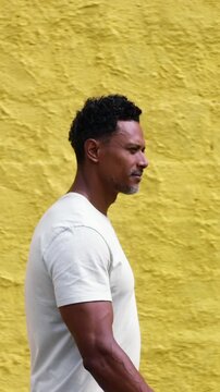 African American man walking along vibrant yellow wall with focused and contemplative gaze