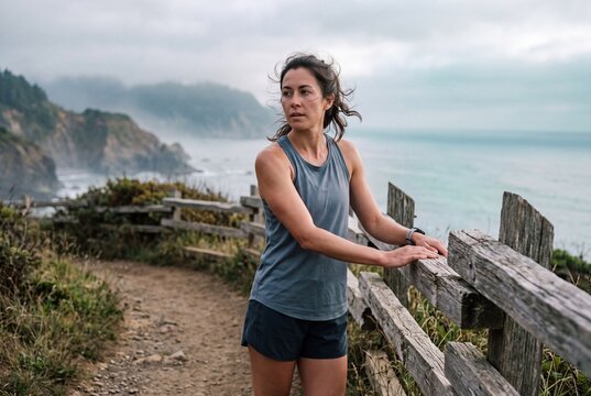 Athletic woman taking a break on a coastal trail overlooking misty ocean cliffs and sea