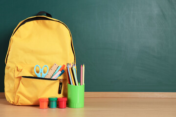 Backpack with stationery on wooden table against chalkboard. Space for text © New Africa