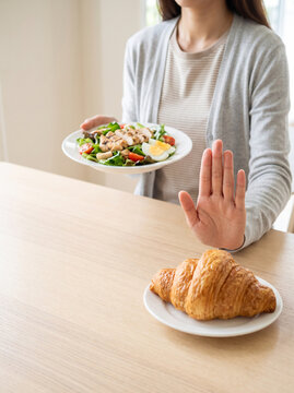 Close up of a woman hand gesturing stop to refuse eating croissant for her weight loss diet program in a bright clean dining room