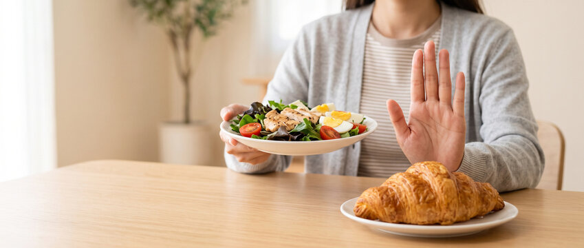 Close up of a woman hand gesturing stop to refuse eating croissant for her weight loss diet program in a bright clean dining room