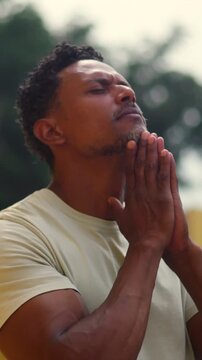 African American man standing outdoors with hands in prayer looking up in contemplation