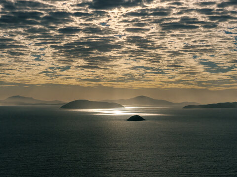 Aerial view of Mistaken Island Nature Reserve surrounded by shimmering ocean waters under a dramatic cloudy sky at sunset in City of Albany, Western Australia, Australia.