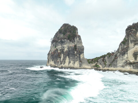 Aerial view of Pangasan Beach featuring a jagged limestone cliff rising from the turquoise sea with crashing waves and lush vegetation in Kecamatan Kebonagung, Jawa Timur, Indonesia.